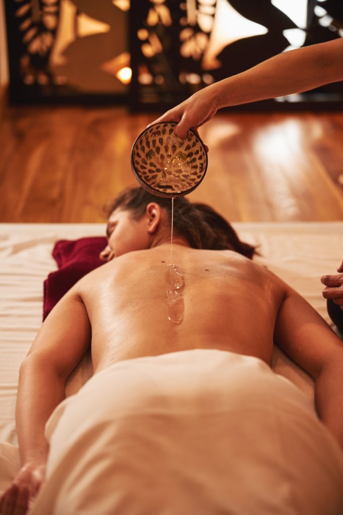 Massage oil flowing from bowl to female skin